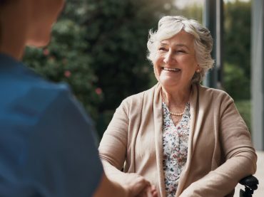 An elderly patient sits holding hands with her nurse